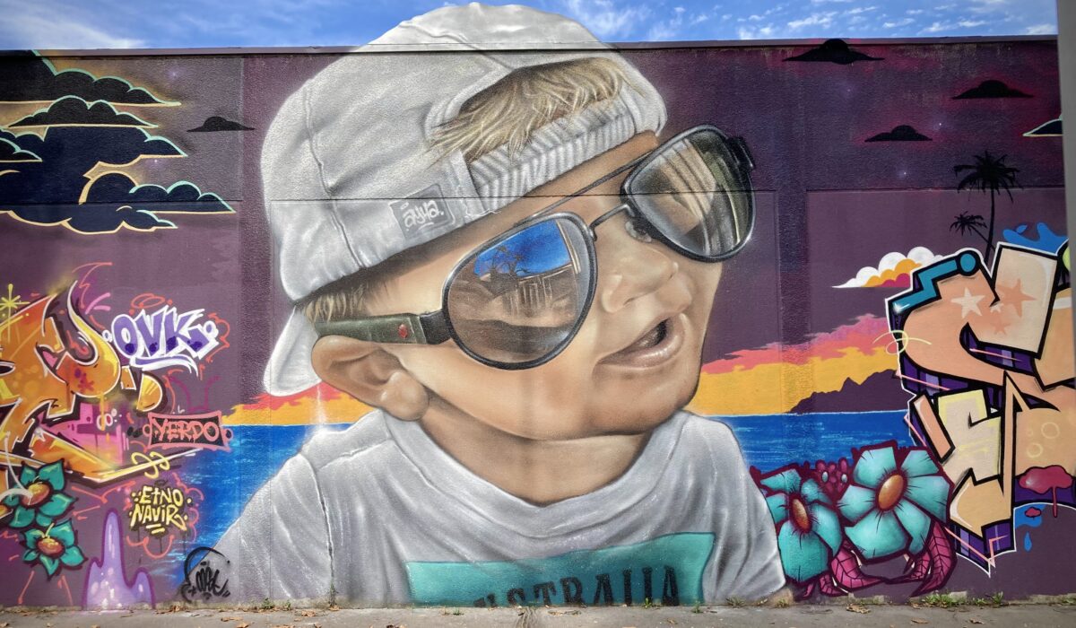 Portrait graffiti réaliste d’un enfant avec lunettes de soleil sur fresque Laguna Beach réalisée lors de la JAM D’ARC 2024 à Cenon.