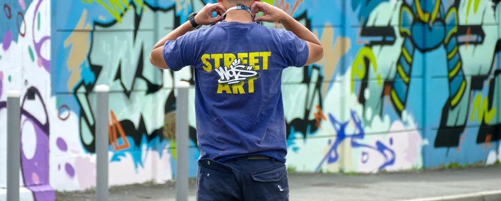 Artiste de dos portant un t-shirt WOLS Street Art devant une fresque graffiti lors de l’événement SLATE 25 à Cenon.